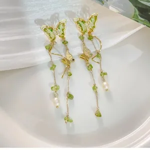 Close-up detail of elegant butterfly tassel earrings featuring green crystals and white pearls.