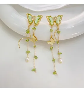 Close-up detail of elegant butterfly tassel earrings with green stones and white pearls