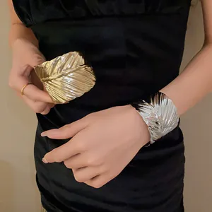 Detailed view showing gold and silver leaf textured wide metal cuff bangles on a model