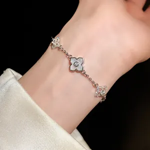 Nahaufnahme eines Silberarmbands mit Zirkon-Kleeblatt und Sternanhängern am Handgelenk.