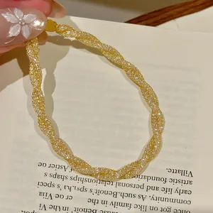 Macro view of an elegant golden twisted mesh bracelet placed on an open book page.
