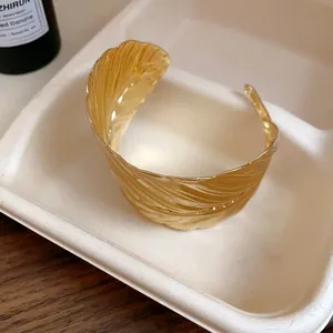 Detailed macro shot of a golden leaf-textured open cuff bracelet on a neutral tray