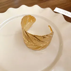 Close-up view of a gold leaf pattern open cuff bracelet resting on an elegant white ceramic plate