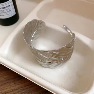 Close-up macro shot of a silver leaf textured metal cuff bracelet on cream tray