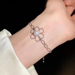 Zartes silbernes Perlenarmband mit einer großen weißen Perlenblume am Handgelenk.