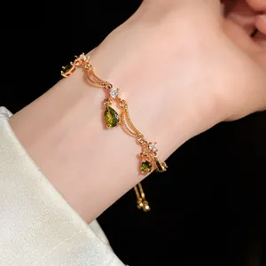 Detailansicht eines eleganten Goldarmbands mit grünen Zirkonia-Tropfen am Handgelenk.