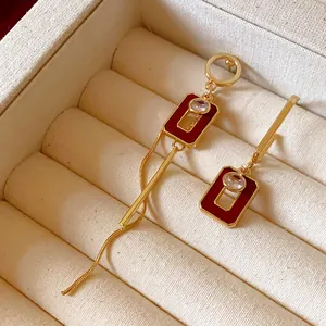 Dettaglio di orecchini asimmetrici in smalto rosso con barre placcate oro in scatola
