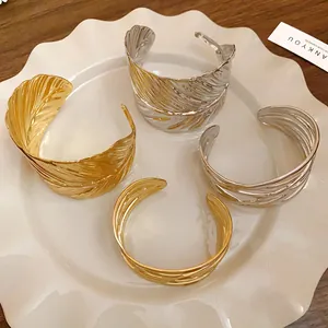 Detailed view of gold and silver metal leaf texture open bracelets on a ceramic plate
