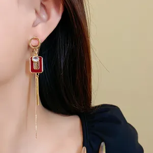 Primo piano di orecchini asimmetrici in smalto rosso stile vintage francese con catena oro.