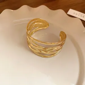 Close-up of a gold-toned open cuff bracelet with an interwoven multi-strand design on a plate.