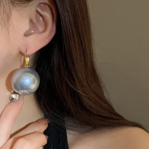Close-up shot of a large greyish-blue pearl hoop earring worn by a model in French style
