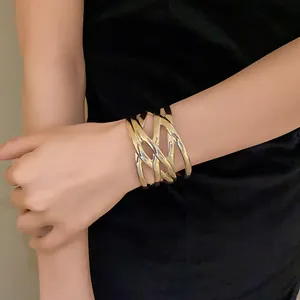 Close-up of a bold gold metal cuff bracelet with a woven leaf-like texture on a model's wrist