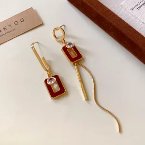Dettaglio di orecchini asimmetrici vintage con smalto rosso e forme geometriche dorate