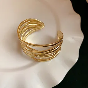 Close-up of a gold metal leaf-textured cuff bracelet on a white decorative plate.