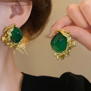 Vintage-style emerald green stud earrings featuring a textured gold frame and silver needles