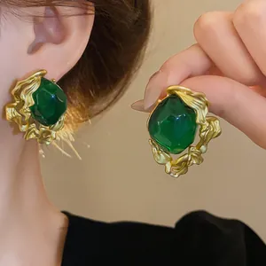 Detailed view of vintage court-style emerald earrings featuring gold textured edges and silver needles