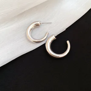 Close-up view of chunky silver-colored C-shaped hoop earrings on textured fabric background