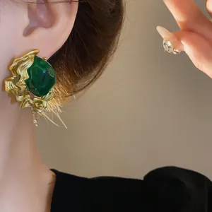 Vintage style emerald green stud earring with ornate golden irregular setting on ear