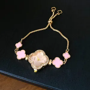Detailansicht eines vergoldeten Uhrenarmbands mit rosa Kleeblatt und Strasssteinen.