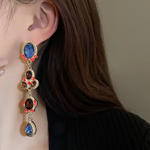 Close-up view of vintage-style dangling earrings with blue and brown stones on an Asian model.