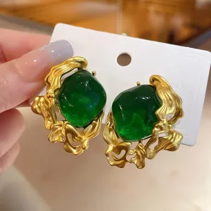 Close-up of vintage emerald green stone earrings with golden irregular metal frames.