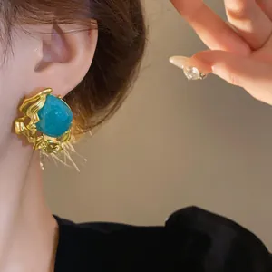 Close-up of vintage gold stud earrings featuring a turquoise green stone and molten metal detail