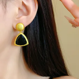 Close-up of vintage gold-tone earrings with black dripping oil enamel and hammered texture.