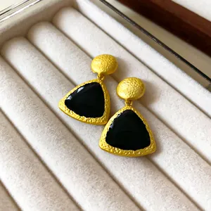 Close-up view of vintage triangular earrings with black enamel and hammered gold texture