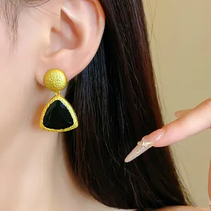 Detailed macro view of vintage gold and black geometric drop earrings on a model ear.