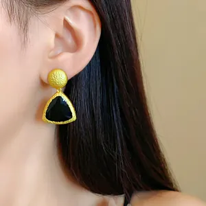 Close-up of vintage gold-toned earring with black geometric triangular pendant