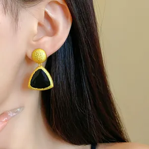 Close-up detail of a vintage gold-tone triangle earring with black enamel on an Asian model