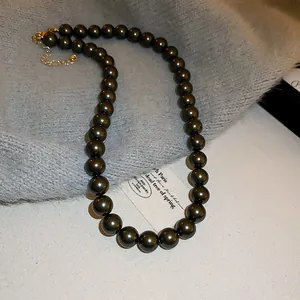 Elegant olive green pearl beaded necklace detail shown on a soft grey textured fabric base.