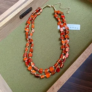 Close-up of double-layer necklace with irregular orange shell pieces and gold beads.