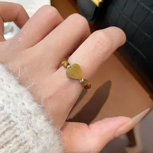 Gros plan d'une bague en perles d'œil de tigre en forme de cœur portée sur un pull moelleux.