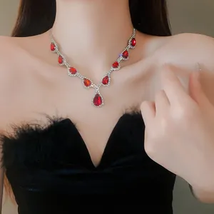 Dettaglio di un'elegante collana di strass rossi a goccia su un abito di piume nere.