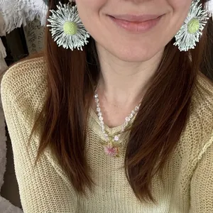 Dettaglio di orecchini a fiore intrecciato verde menta e collana di perle con ciondolo.