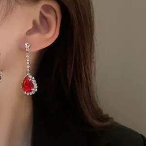 Primo piano di un elegante orecchino a goccia con gemma rossa vibrante e strass