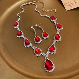 Dettaglio del set di collana e orecchini con strass rossi a goccia su piatto dorato.