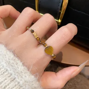 Gros plan d'une bague rétro en perles d'œil de tigre avec une breloque cœur au doigt