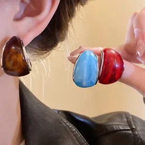 Primer plano de pendientes de resina en forma de C en colores ámbar, azul y rojo.