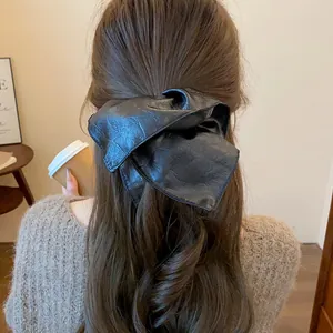 Back view of a woman wearing a black leather oversized bow scrunchie on wavy hair
