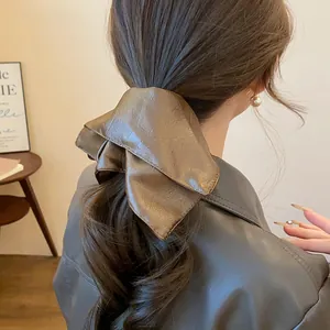 Detail of a brown leather scrunchie tied on a wavy ponytail hair style
