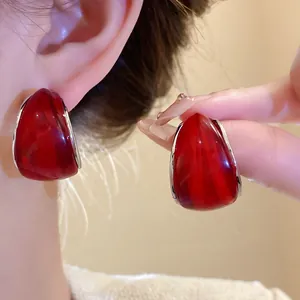 Detalle de pendientes de aro en forma de C de resina roja con pasadores de plata, retro.