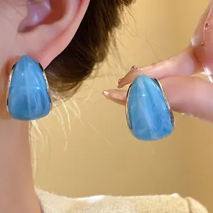 Primer plano de pendientes de resina azul en forma de C con textura de mármol y plata