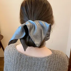 Detailed view of a stylish large silver metallic leather scrunchie on a low bun hairstyle