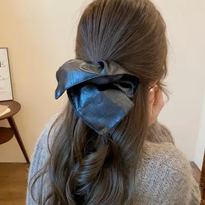 Close-up of a stylish black faux leather oversized scrunchie on long wavy brown hair