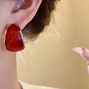 Detalle de elegante pendiente de resina roja en forma de C con borde metálico plateado