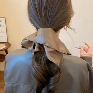 Close-up of oversized textured brown leather scrunchie with vintage square design on hair