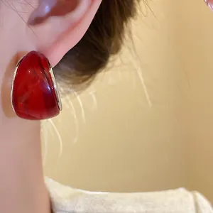 Primer plano de un pendiente de resina roja en forma de C con aguja de plata en la oreja