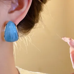 Primer plano detallado de pendientes de aro de resina azul en forma de C en una modelo